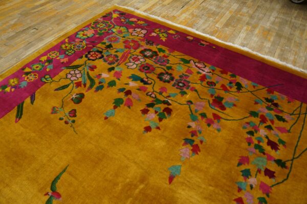 Golden yellow rug with a fuchsia border and multicolored floral pattern resting on distressed wood flooring.