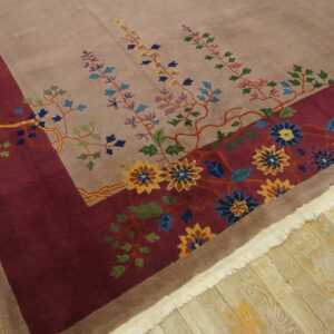 Multicolor floral patterns cover a taupe rug with a wide burgundy border on light wood floors.