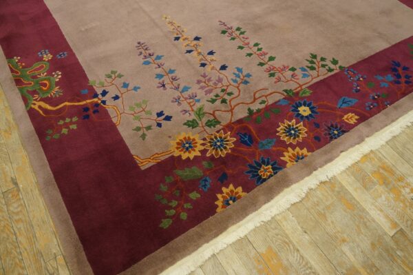 Multicolor floral patterns cover a taupe rug with a wide burgundy border on light wood floors.