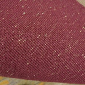 Detailed view of a deep red, diagonally woven textile speckled with light beige fibers.