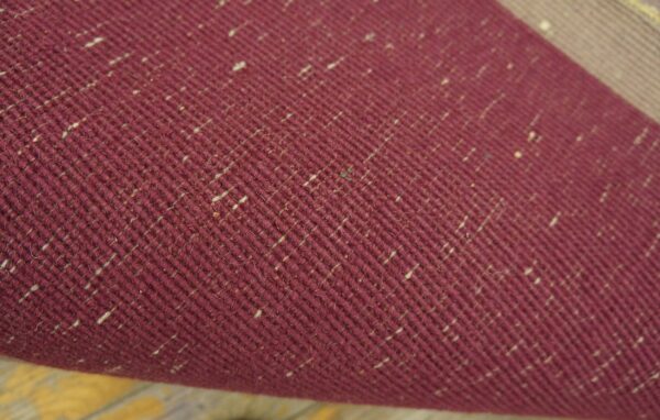 Detailed view of a deep red, diagonally woven textile speckled with light beige fibers.