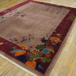 Mauve rug with colorful floral motifs on a wide burgundy border, placed on worn wooden floorboards.