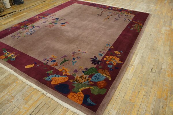 Mauve rug with colorful floral motifs on a wide burgundy border, placed on worn wooden floorboards.