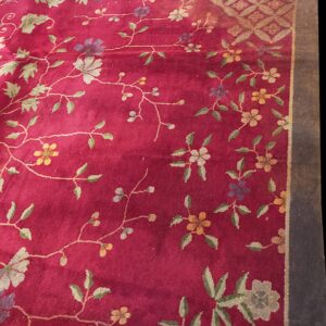 Rich red floral rug featuring subtle green, yellow, and purple blossoms with a golden geometric corner detail.