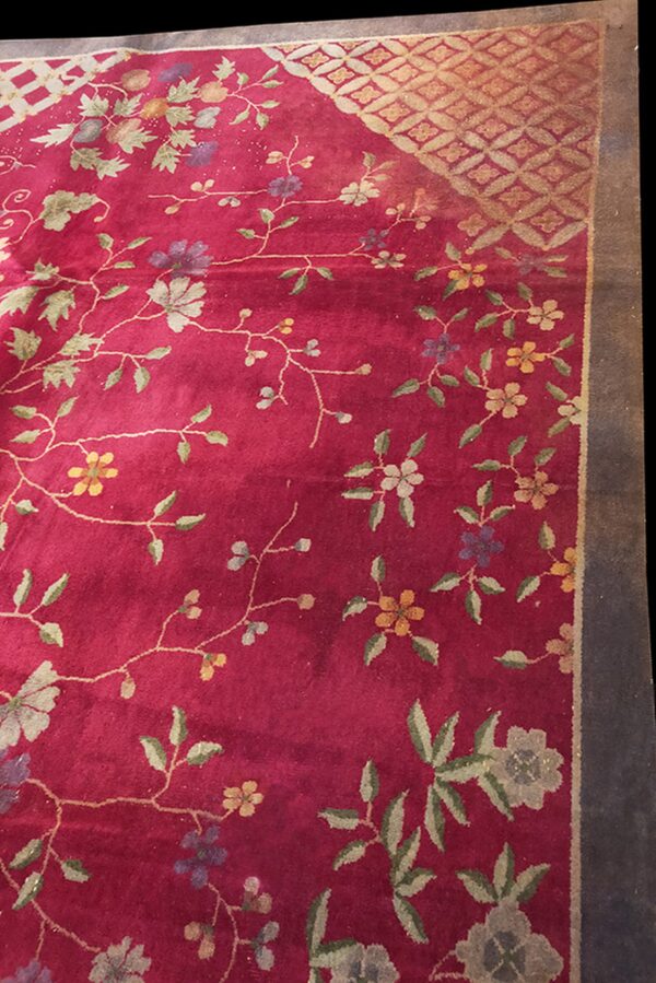 Rich red floral rug featuring subtle green, yellow, and purple blossoms with a golden geometric corner detail.