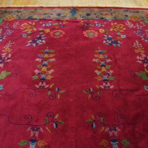 Plush deep pink rug featuring multi-colored floral designs and a wide gray-brown border on golden wood floors.