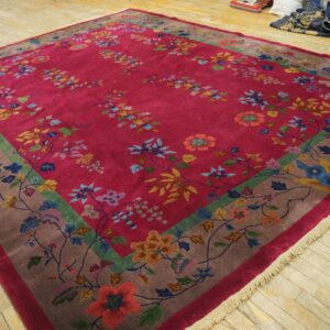 High-pile magenta rug with scattered multicolor florals and a decorative wide taupe and green border on wood planks.