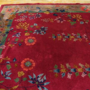 Deep red rug with complex floral patterns in blue, yellow, and green on light wood floors.