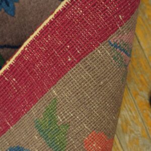 Folded floral rug shows the gray patterned face and a wide magenta flatweave edge on distressed yellow wood.