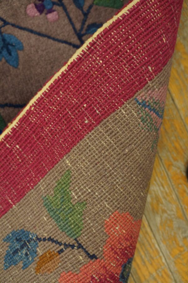 Folded floral rug shows the gray patterned face and a wide magenta flatweave edge on distressed yellow wood.