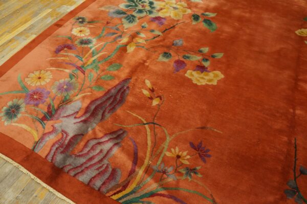Close-up of a plush rust orange rug featuring colorful yellow and purple floral and abstract designs on wood flooring.
