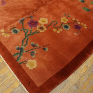 Orange rug with floral branches and a dark rust border resting on distressed wood planks.
