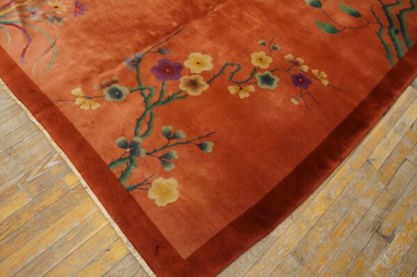 Orange rug with floral branches and a dark rust border resting on distressed wood planks.
