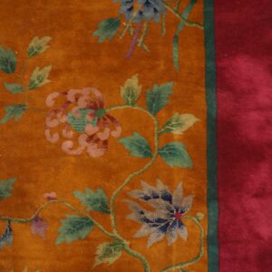 Burnished orange rug detail shows floral vines and a wide, solid red border next to wood flooring.