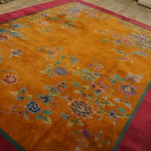 High-pile orange rug with scattered colorful flowers and a wide pink border on distressed wood flooring.