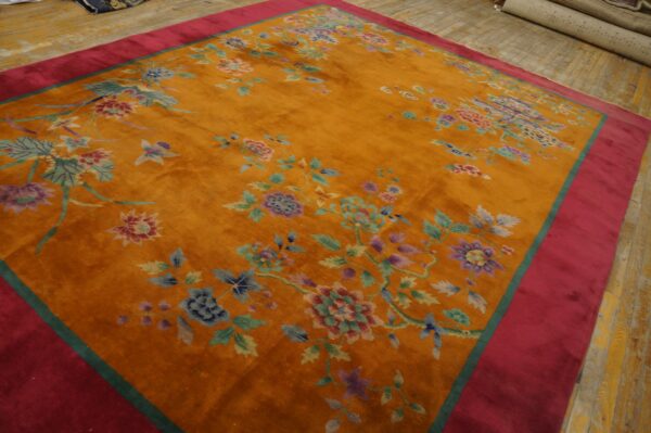 High-pile orange rug with scattered colorful flowers and a wide pink border on distressed wood flooring.