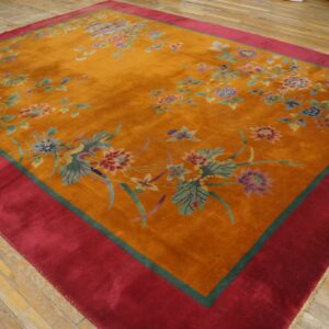 Plush orange rug with scattered pastel floral motifs and a wide red border on rustic wooden planks.