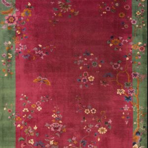 Ornate rug with a magenta center field and green border decorated with intricate floral patterns.