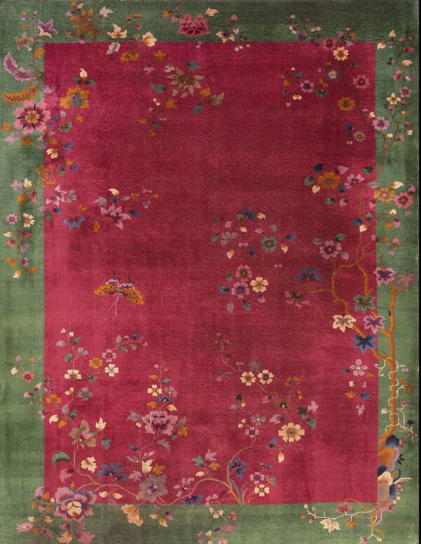 Ornate rug with a magenta center field and green border decorated with intricate floral patterns.