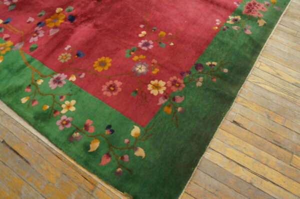 Magenta rug with colorful flowering branches and a bright green border sits on yellow wood floorboards.
