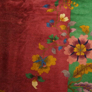 Red and green plush rug featuring a colorful vine and floral pattern on light wooden plank flooring.