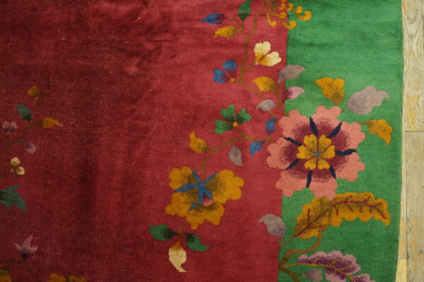 Red and green plush rug featuring a colorful vine and floral pattern on light wooden plank flooring.