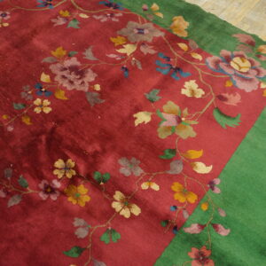 Vibrant red rug featuring a sprawling floral pattern, bordered in solid green on wood plank floor.