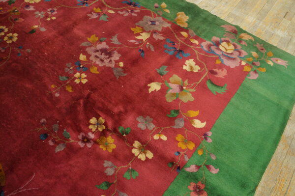 Vibrant red rug featuring a sprawling floral pattern, bordered in solid green on wood plank floor.