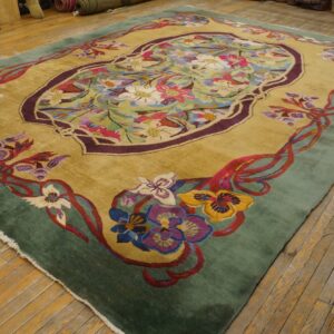 Gold rug featuring a multicolored floral medallion, sage green border, and lying on wooden floorboards.