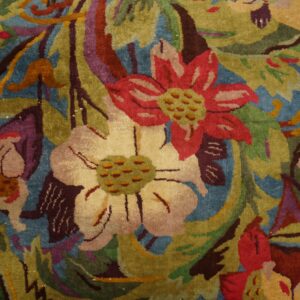 Textured rug close-up showing a dense design of red, cream, and green flowers against a deep blue ground.