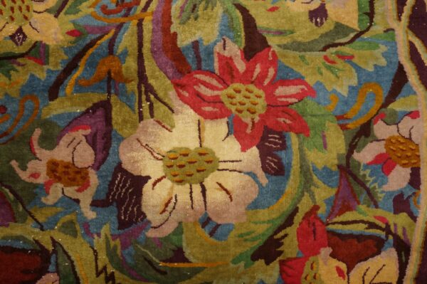 Textured rug close-up showing a dense design of red, cream, and green flowers against a deep blue ground.