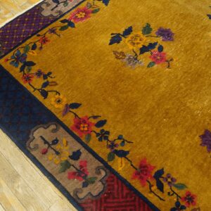Mustard yellow rug featuring multicolored floral sprays and layered navy, purple, and brown borders on wood flooring.