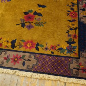 Mustard yellow rug with red and blue floral patterns and complex borders rests on light wood planks.
