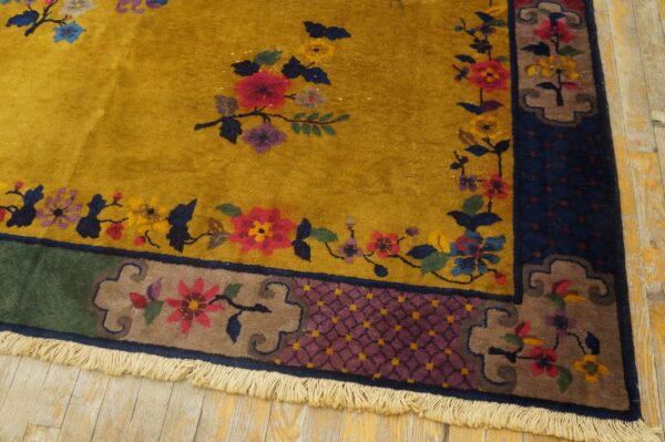 Mustard yellow rug with red and blue floral patterns and complex borders rests on light wood planks.