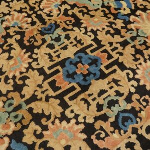 Black rug with large tan scrolling floral motifs, blue accents, and geometric fretwork on wood floor.