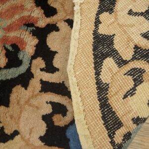 Close-up of a high-pile rug with black, tan, and blue colors exposing its woven geometric backing.