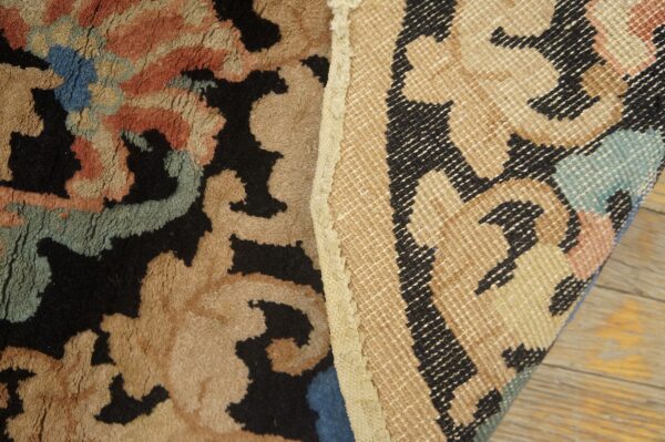 Close-up of a high-pile rug with black, tan, and blue colors exposing its woven geometric backing.