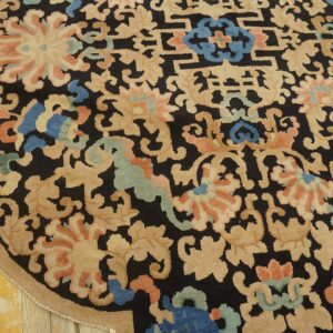 Rounded black rug with dense beige, coral, and blue floral patterns rests on distressed wood flooring.