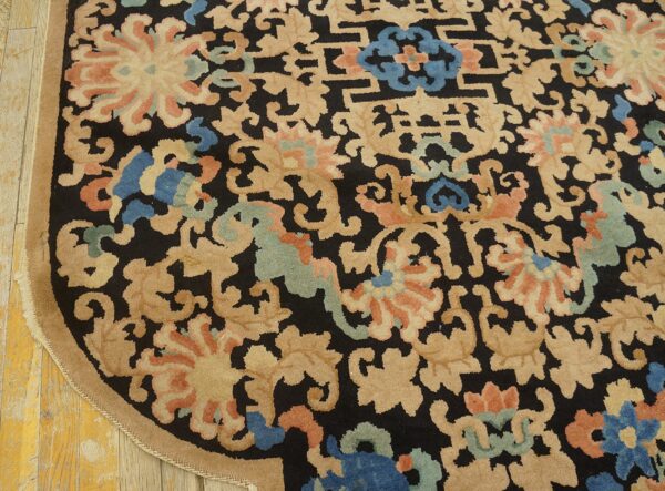 Rounded black rug with dense beige, coral, and blue floral patterns rests on distressed wood flooring.