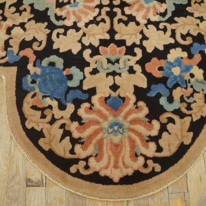 Rounded rug edge with black, beige, blue, and terracotta floral designs on rustic plank flooring.