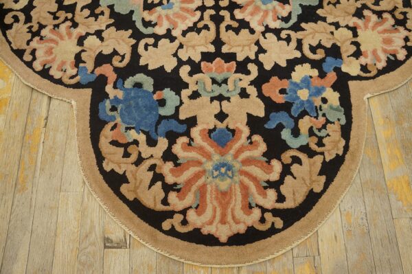 Rounded rug edge with black, beige, blue, and terracotta floral designs on rustic plank flooring.