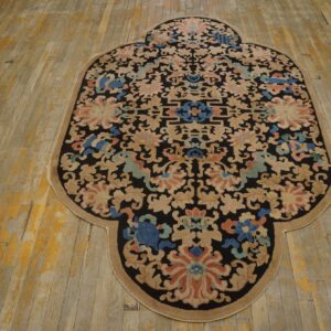 A lobed rug featuring black, tan, coral, and blue floral patterns rests on distressed wood plank flooring.