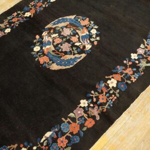 Black rug with a colorful floral border and central bird medallion on light hardwood floors.