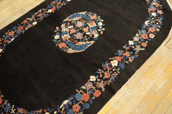Black rug with a colorful floral border and central bird medallion on light hardwood floors.