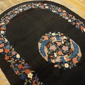 Black oval rug with a floral border and central bird medallion on light wood flooring.