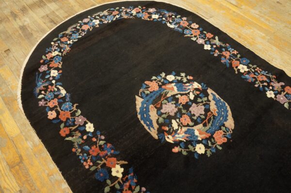Black oval rug with a floral border and central bird medallion on light wood flooring.