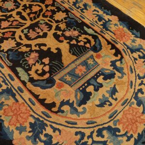 Ornate oval rug with tan, blue, and coral botanical patterns on a dark ground over wood planks.