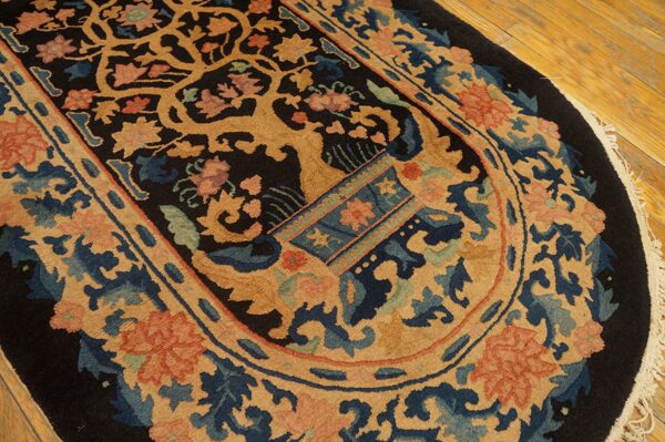 Ornate oval rug with tan, blue, and coral botanical patterns on a dark ground over wood planks.