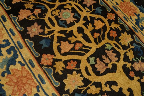 The rug features an intricate floral vine design in gold, coral, and blue on a textured black background.