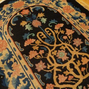 Ornate black rug with a curvilinear gold vine pattern and floral motifs in coral, blue, and tan on wood planks.